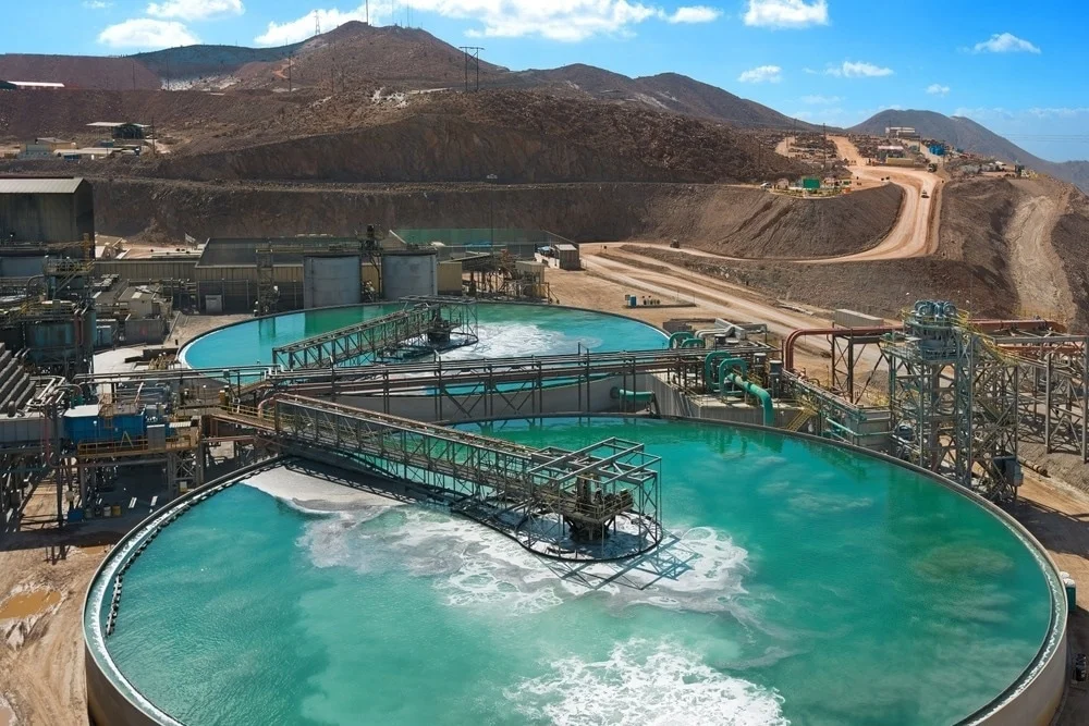 Sustainable mining operation with advanced water management systems in place, showing large circular water treatment tanks at a mining facility surrounded by a mountainous landscape.