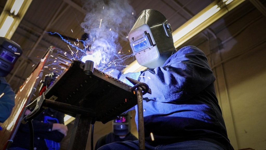 Welder at work, wearing protective gear, sparks flying during a metal welding process.