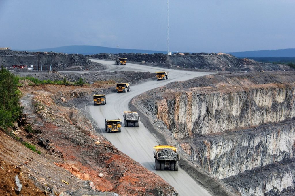 Large haul trucks transporting metal ore along winding roads at an open-pit mining site.