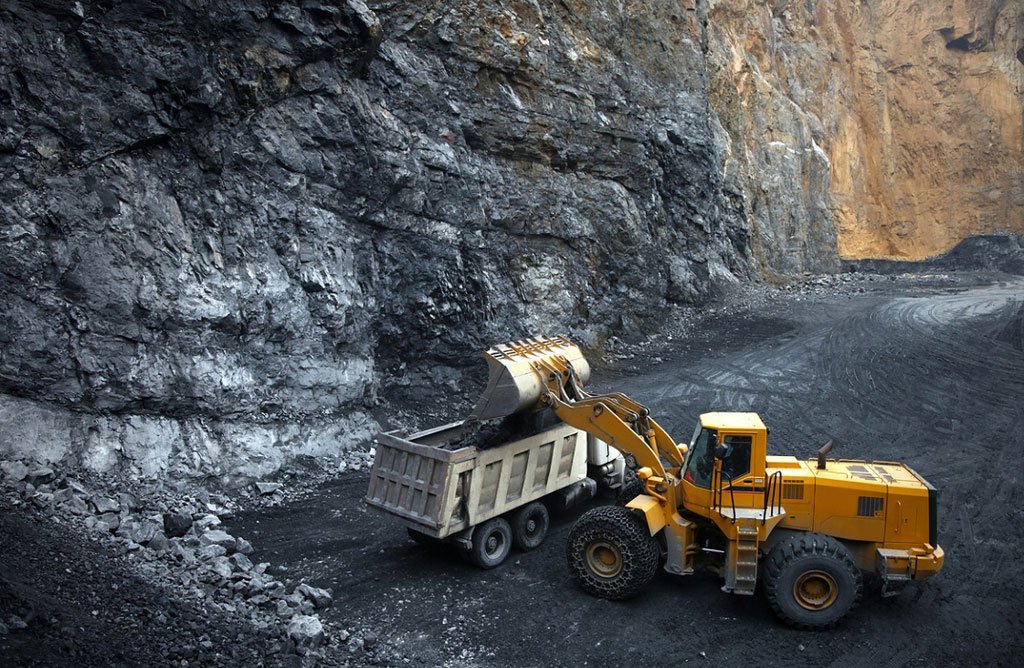 Excavator loading a truck with metal ore at a mining site inside a large rock quarry.