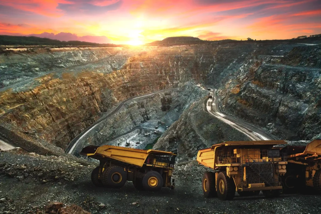 Open-pit mining site at sunset with large haul trucks navigating the winding pathways, illustrating the scale and operations of modern mining.
